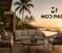 Luxury outdoor patio furniture by Mod Patio at a premium resort, featuring sofas and woven lounge chairs overlooking a pool and sunset.